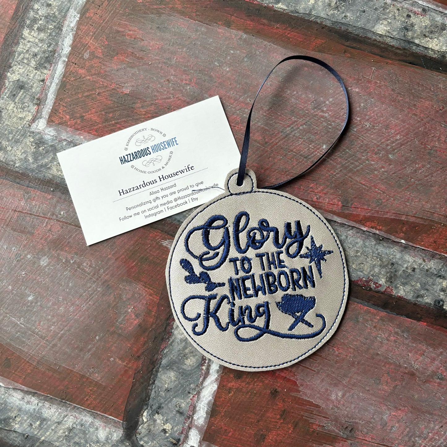 Round embroidered pendant with 'Glory to the Newborn King' text on a wooden surface