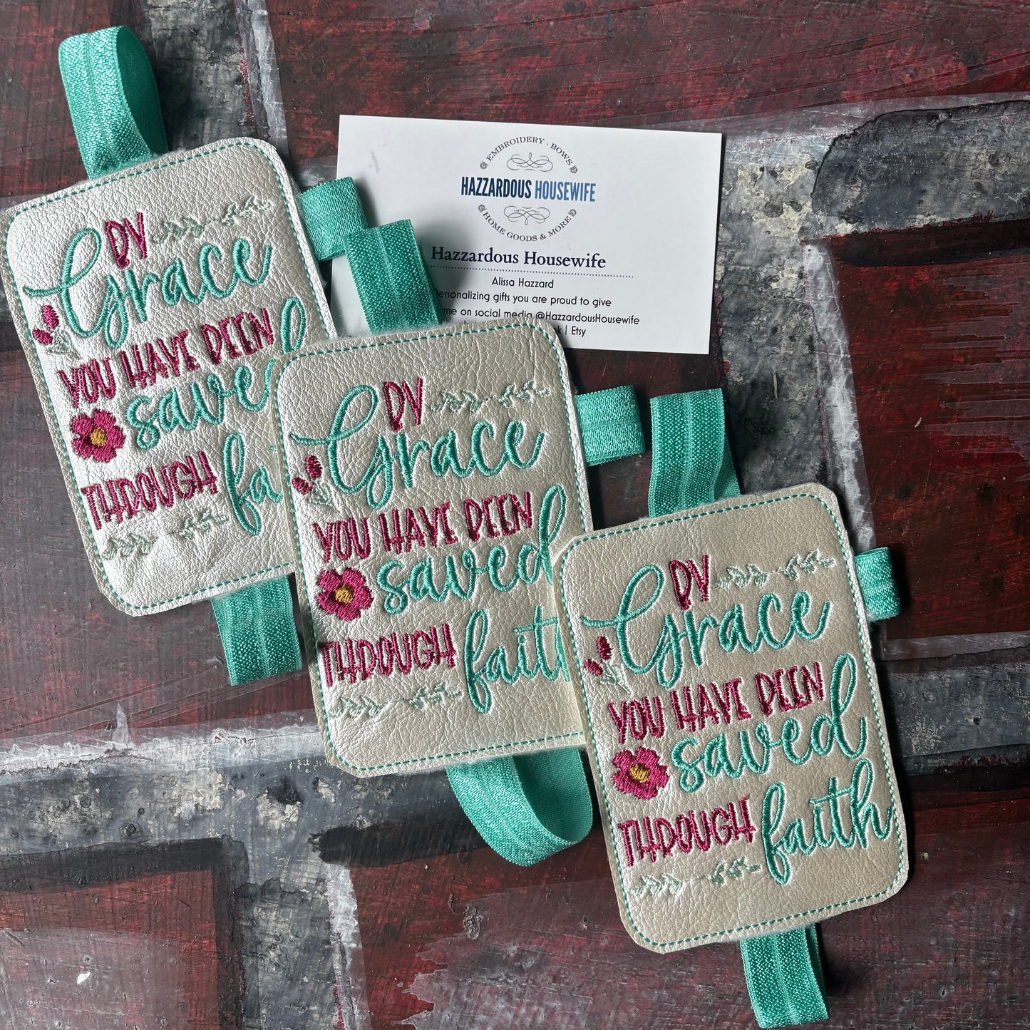 Three embroidered book bands with pen holder and motivational text on a rustic wooden surface.