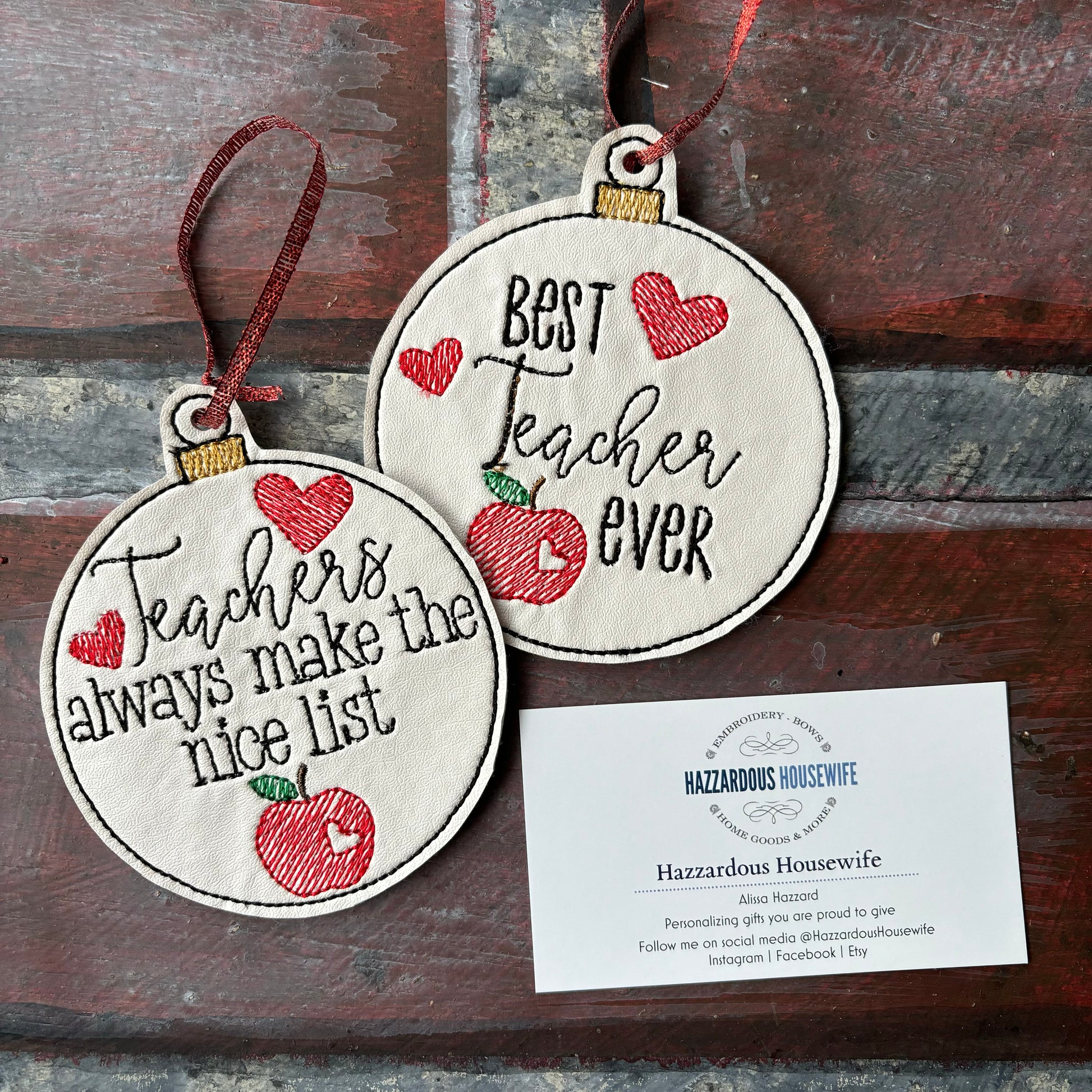 Two round ornaments with text and an apple design on a wooden surface, accompanied by a business card.