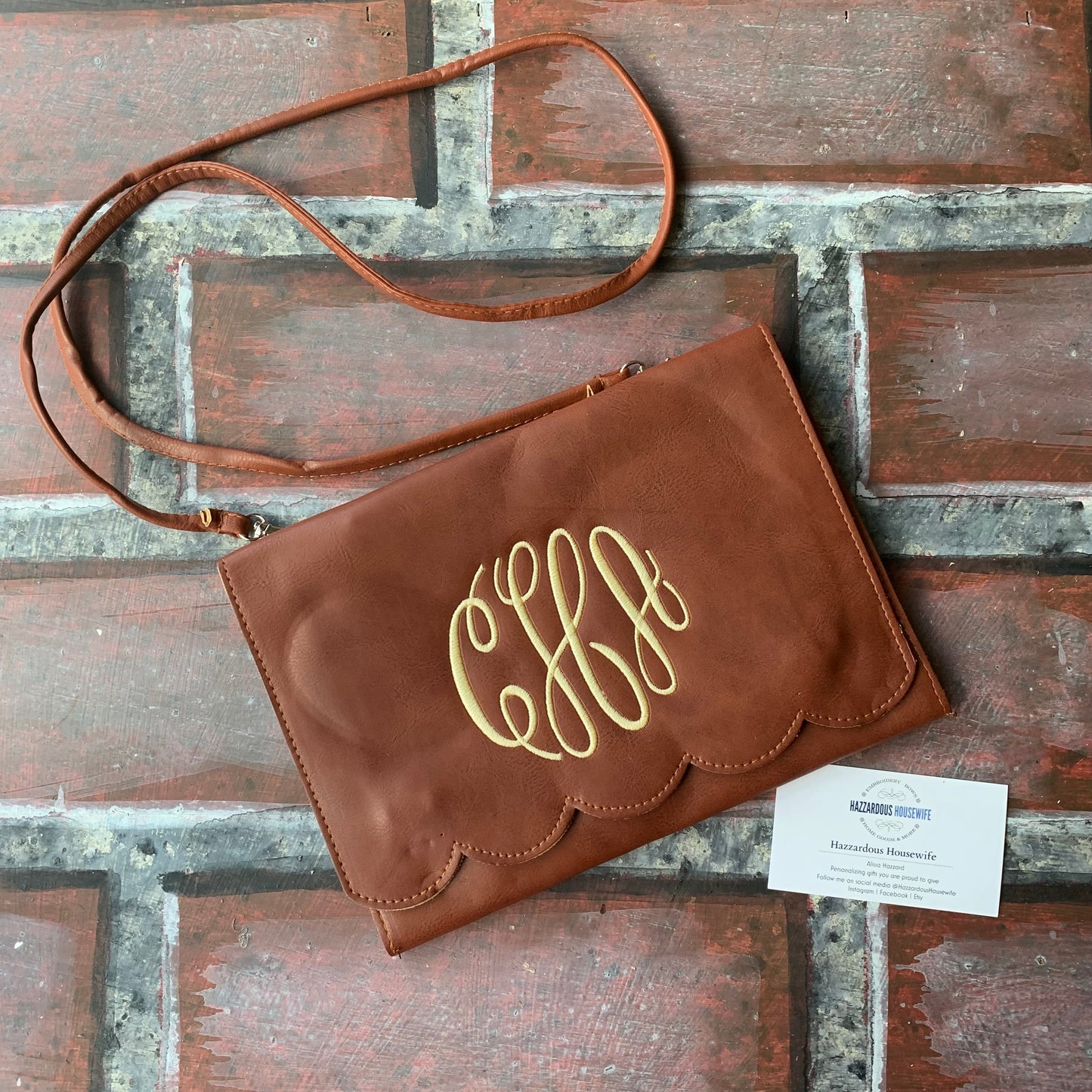 Brown clutch bag with gold monogram on a wooden surface