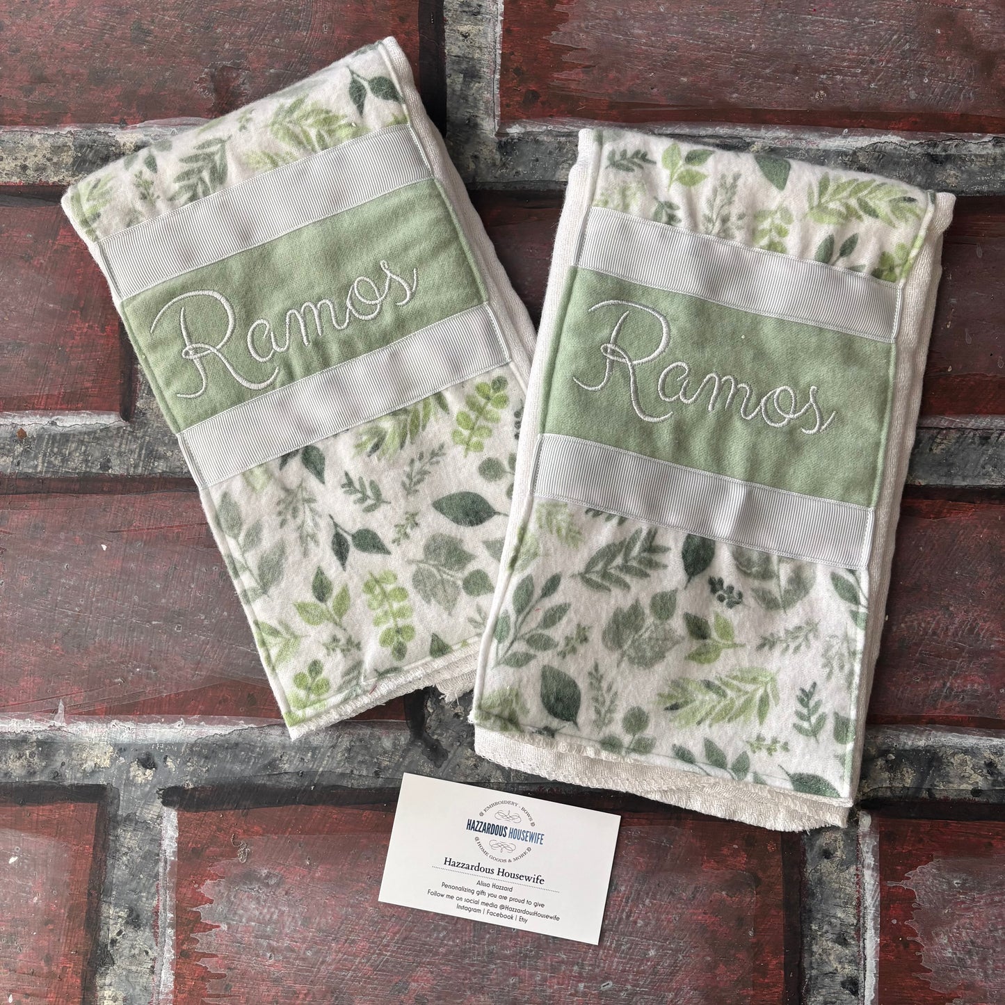 Two green and white patterned burp cloths with personalized branding on a brick surface.