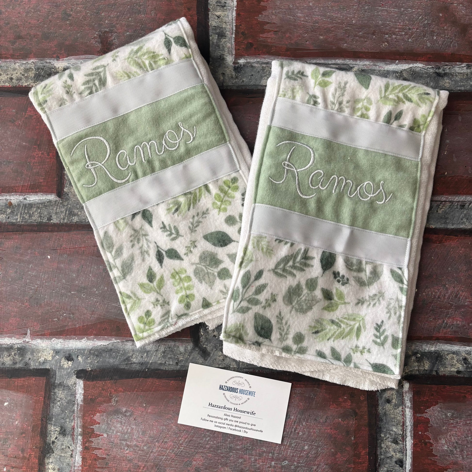 Two green and white patterned burp cloths with personalized branding on a brick surface.