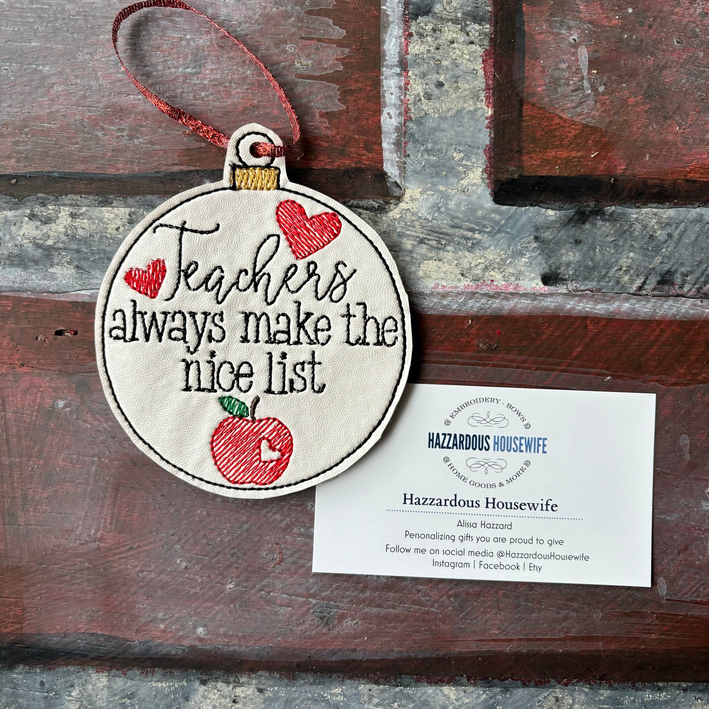 Decorative ornament with 'Teachers always make the nice list' text and an apple illustration on a wooden surface with a business card.
