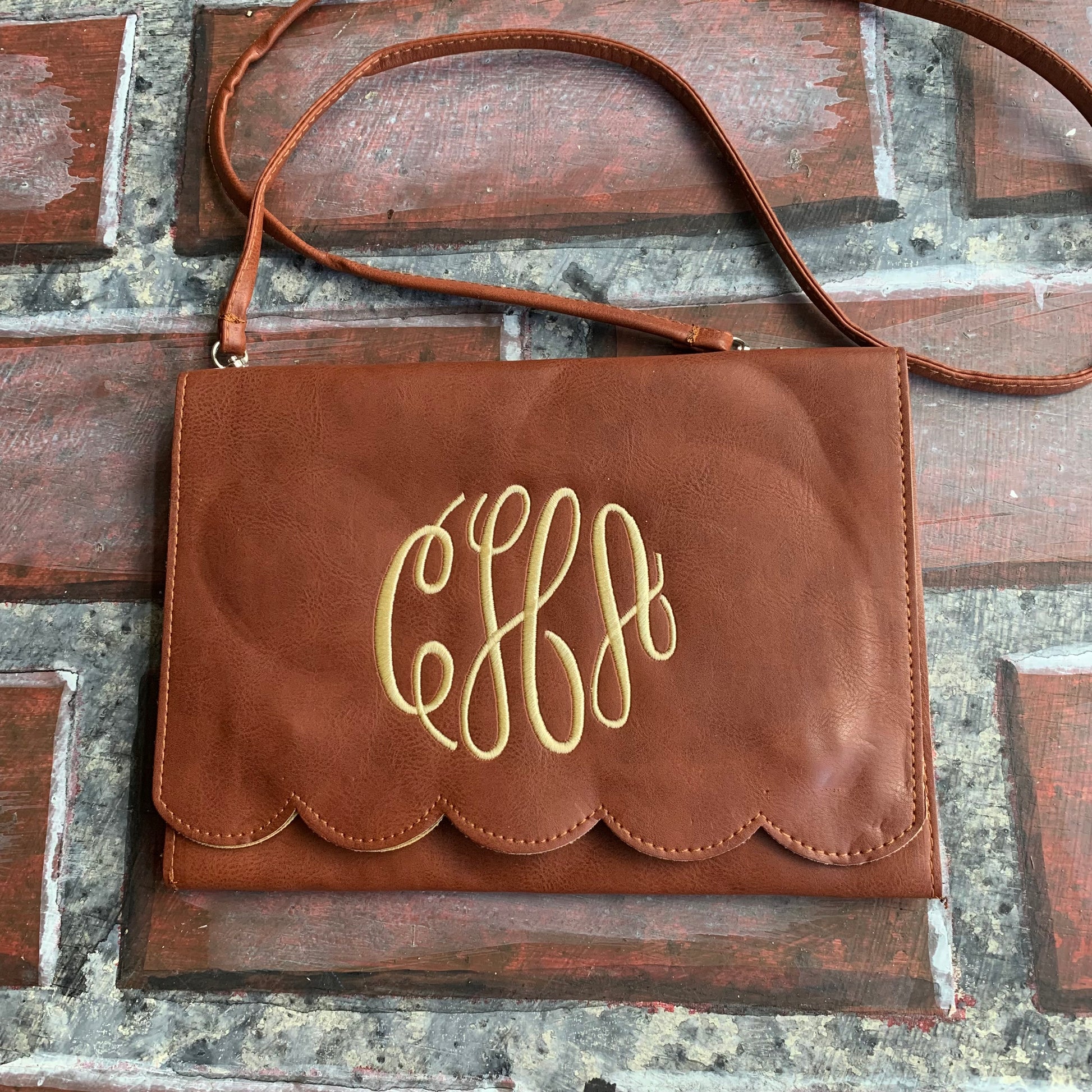 Brown leather handbag with gold monogram on a brick wall background