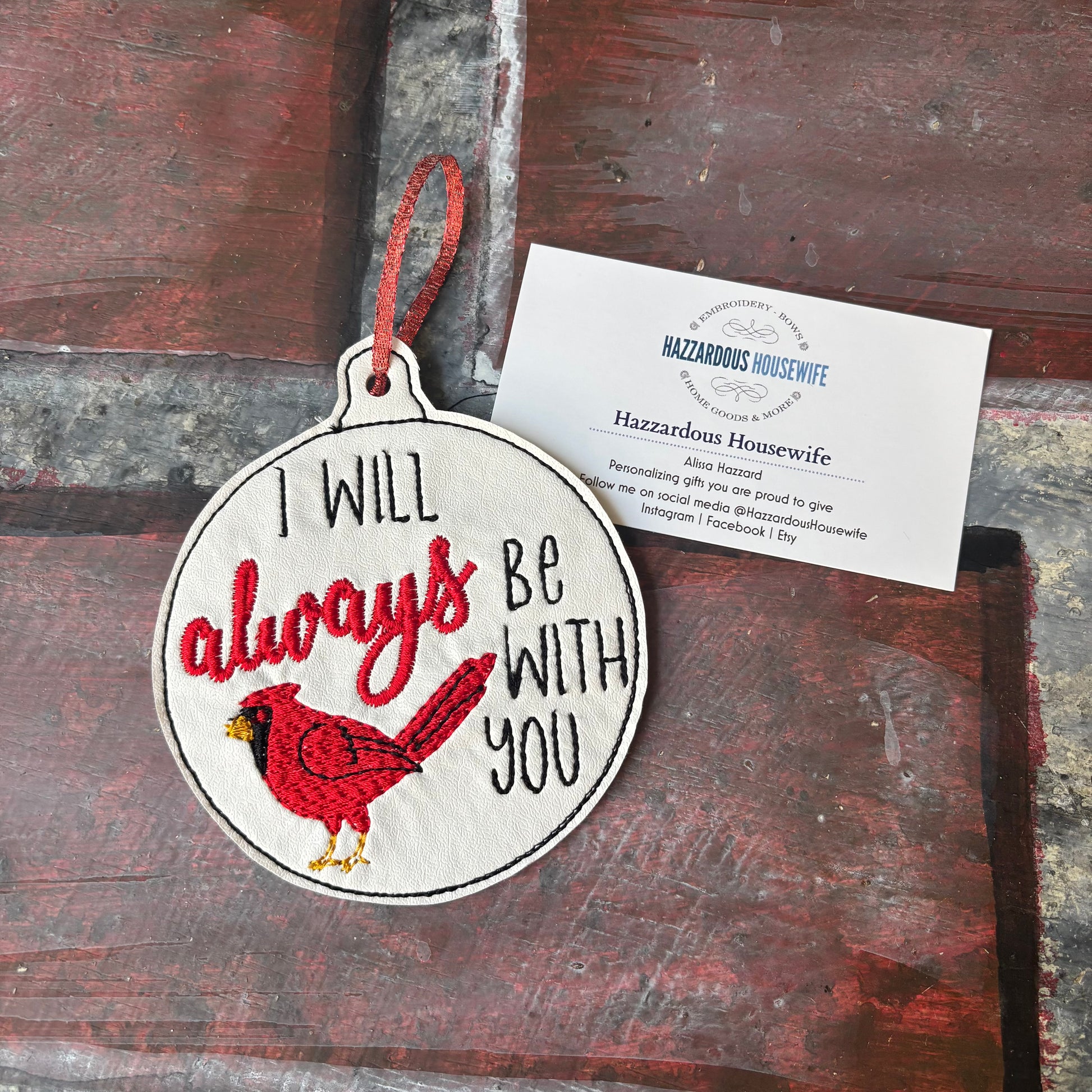 Decorative ornament with red cardinal and text 'I will always be with you' on a rustic wooden surface.