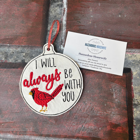 Decorative ornament with red cardinal and text 'I will always be with you' on a rustic wooden surface.