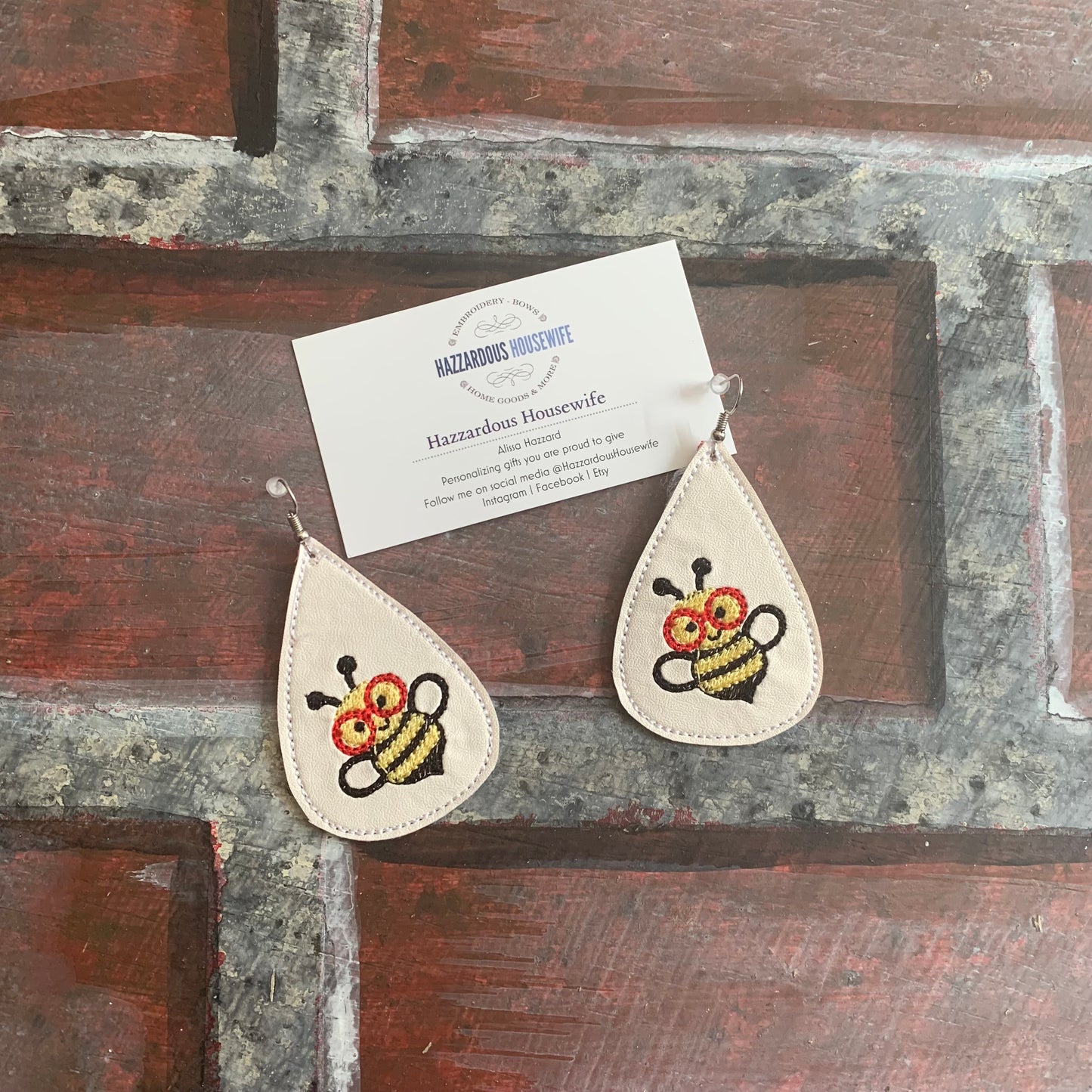 Teardrop-shaped earrings with bee design on a rustic wooden surface.