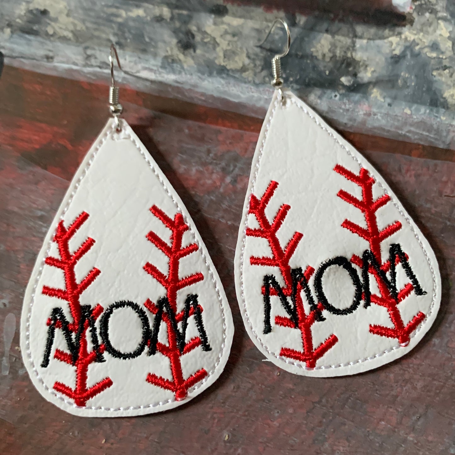 Teardrop-shaped earrings with 'MOM' embroidery on a wooden surface