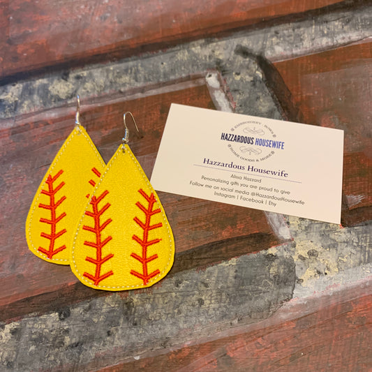 Yellow earrings with red patterns on a wooden surface with a HazzardousHouswife business card.