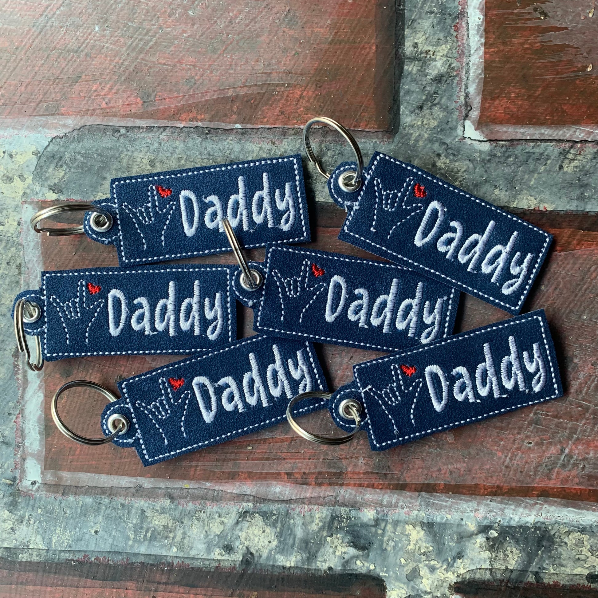 Multiple 'Daddy' keychains on a textured wooden surface