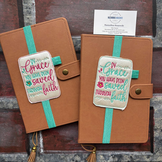 Two brown leather journals with embroidered patches and teal straps for a book band on a rustic wooden surface.