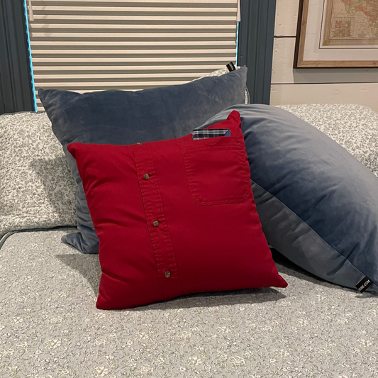 Red Memory pillow on a bed with gray and blue pillows, in a room setting.